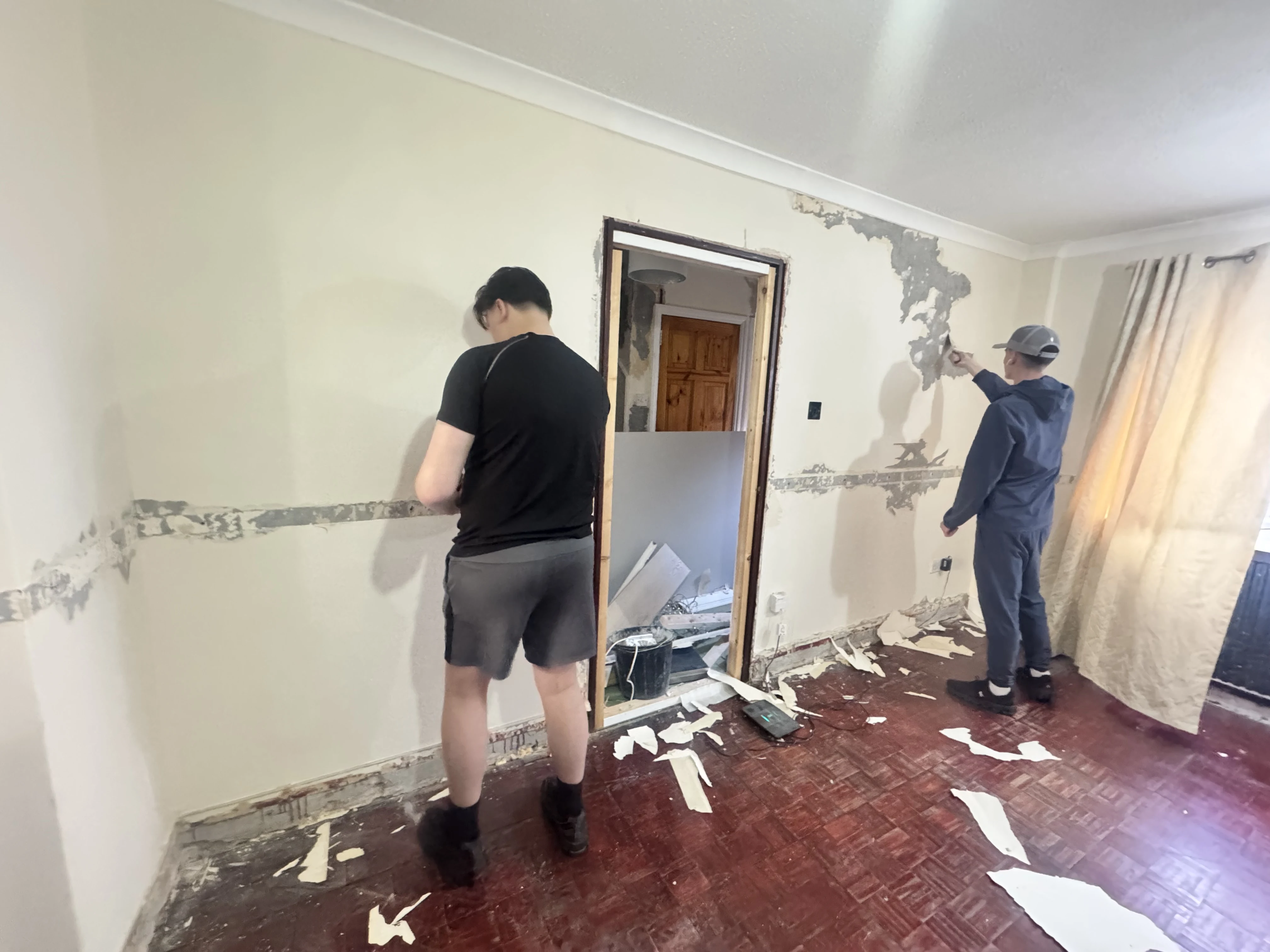 Two Community Heroes volunteers stripping wallpaper in a resident's home