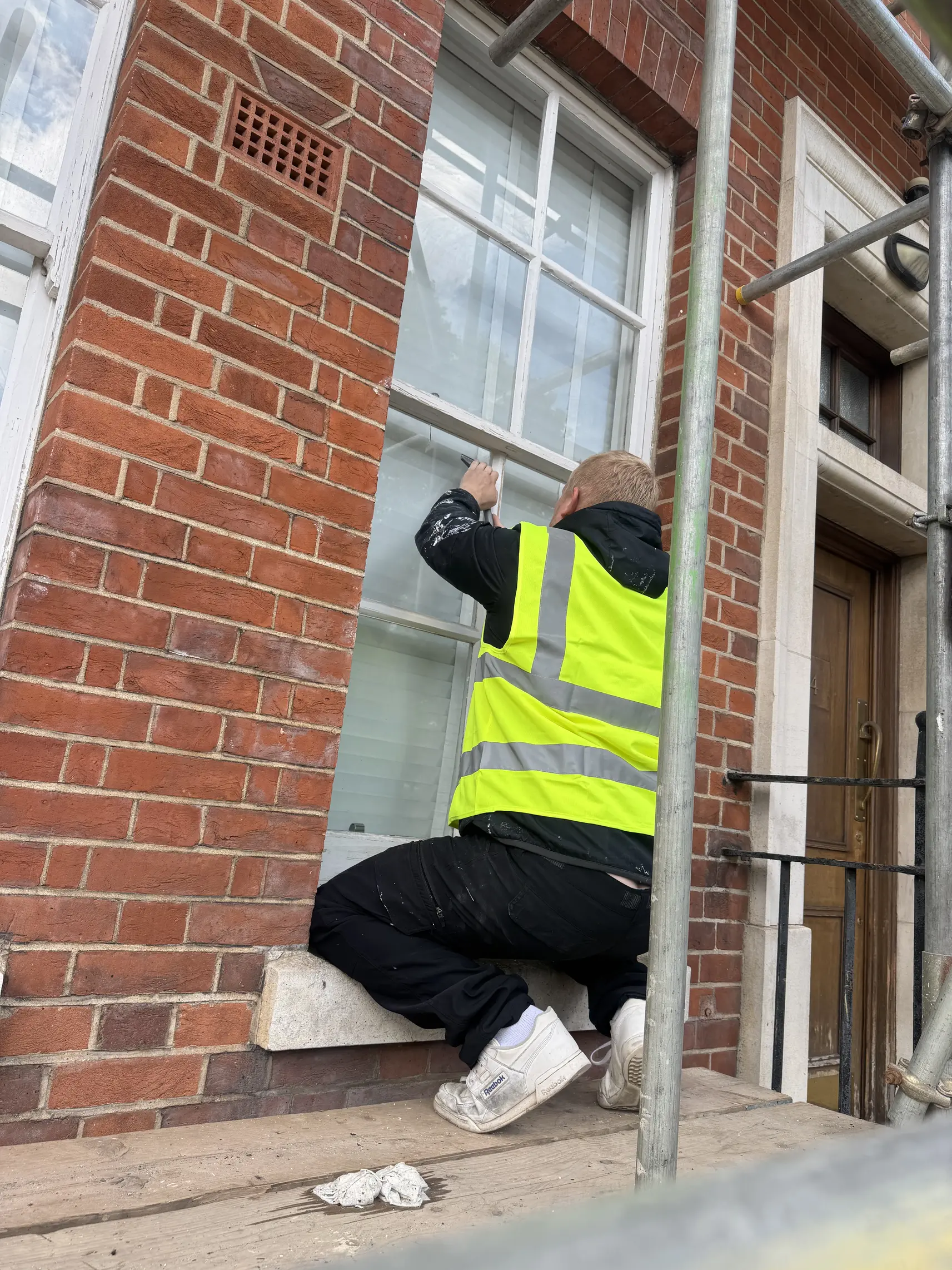 Community Heroes volunteer in hi-vis carrying out window repairs on scaffolding